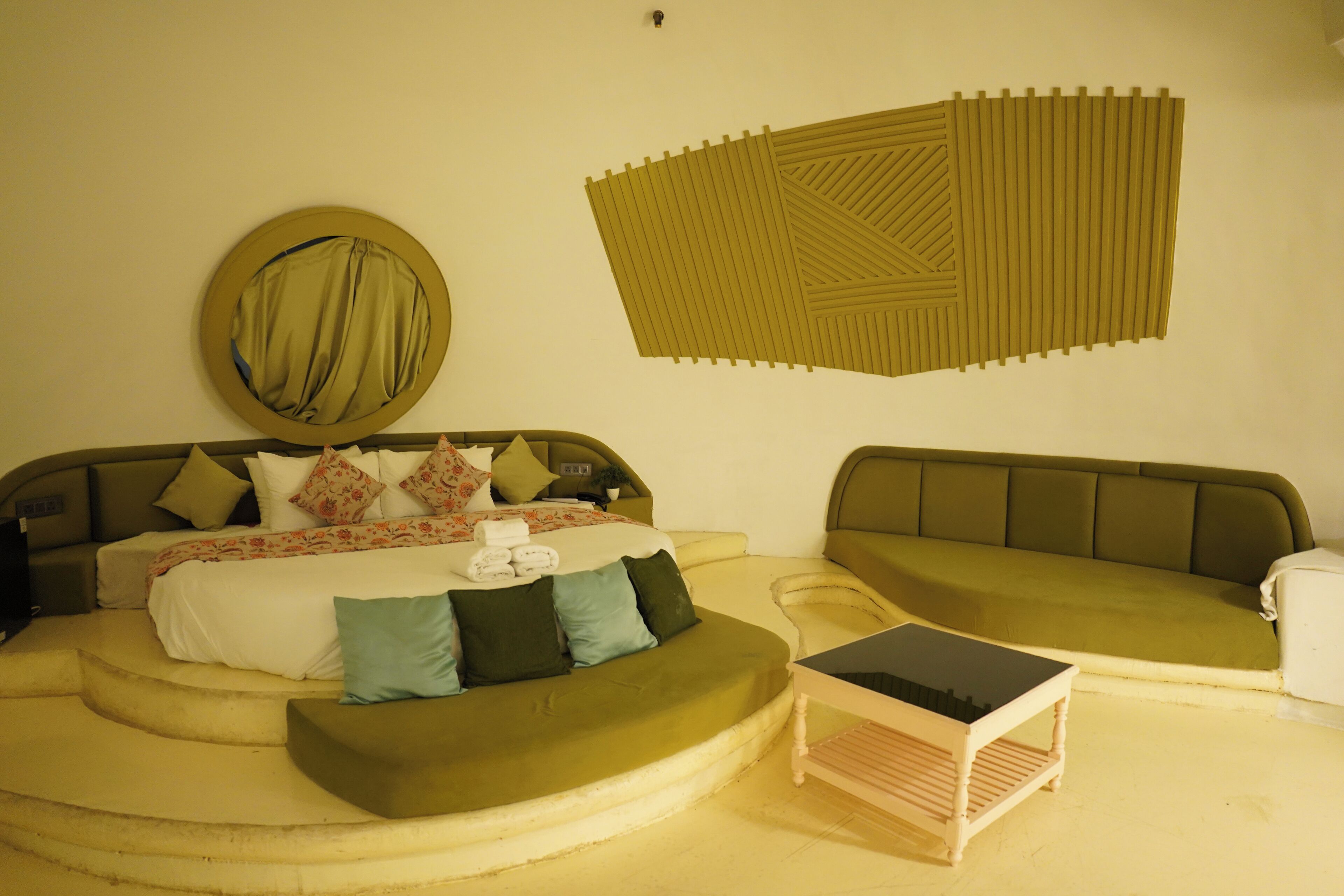 Une pièce comprenant un lit à la forme arrondie, un canapé, une petite table et un panneau décoratif fixé au mur.