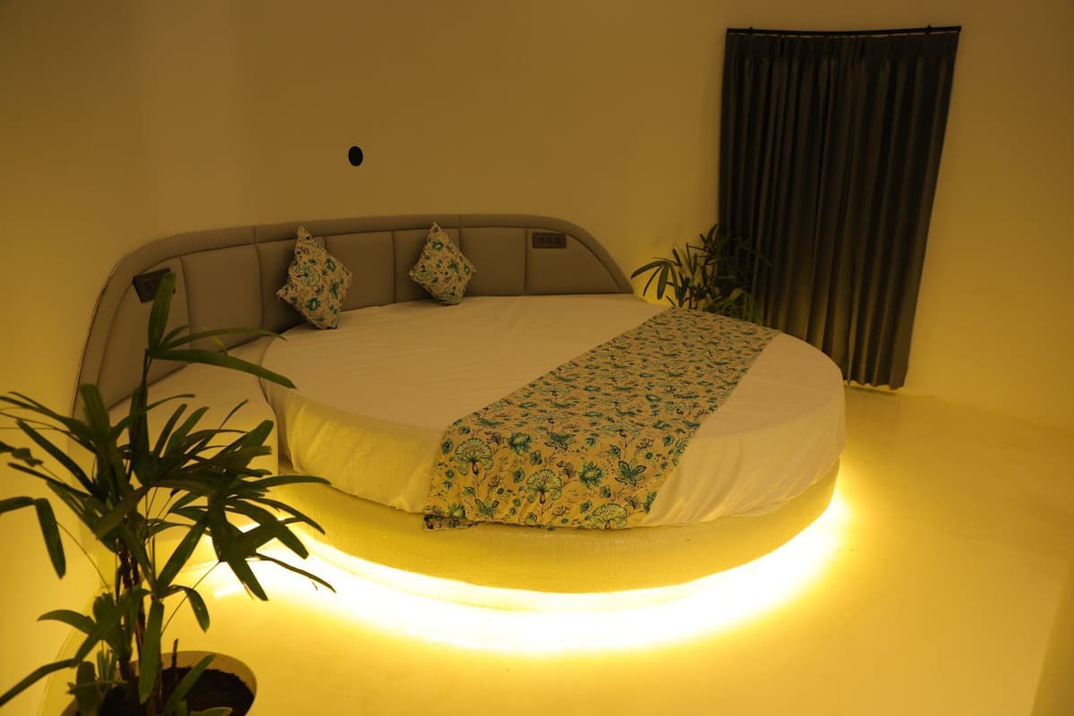 A bed with a floral bedspread, a headboard, and a bedside plant.