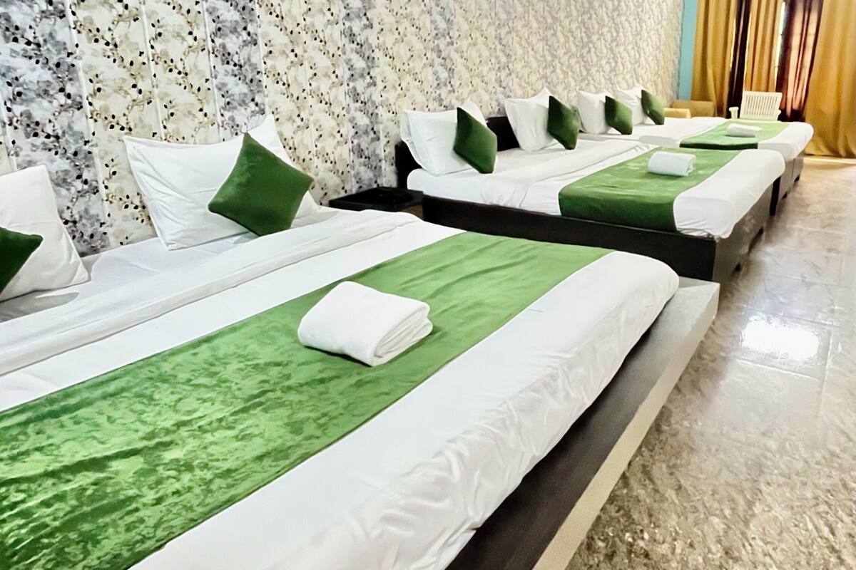 A row of neatly arranged beds with green and white linens, a marble floor, and a patterned wall in the background.