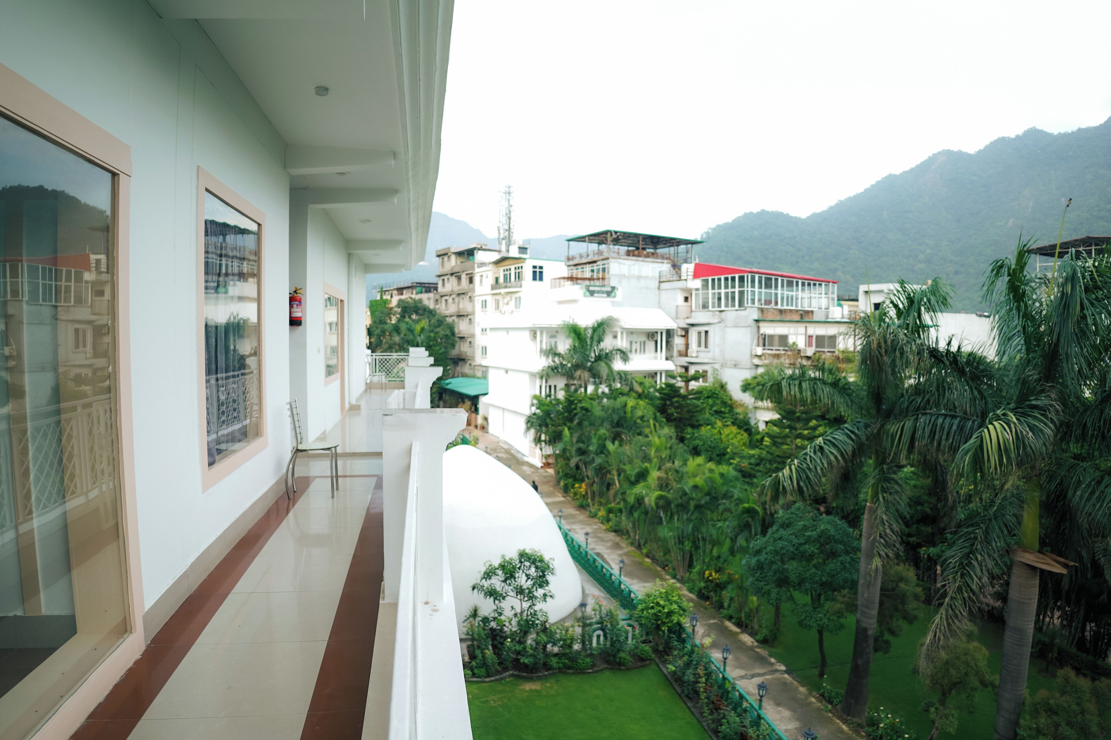 Un balcon donnant sur un jardin luxuriant et les bâtiments environnants.