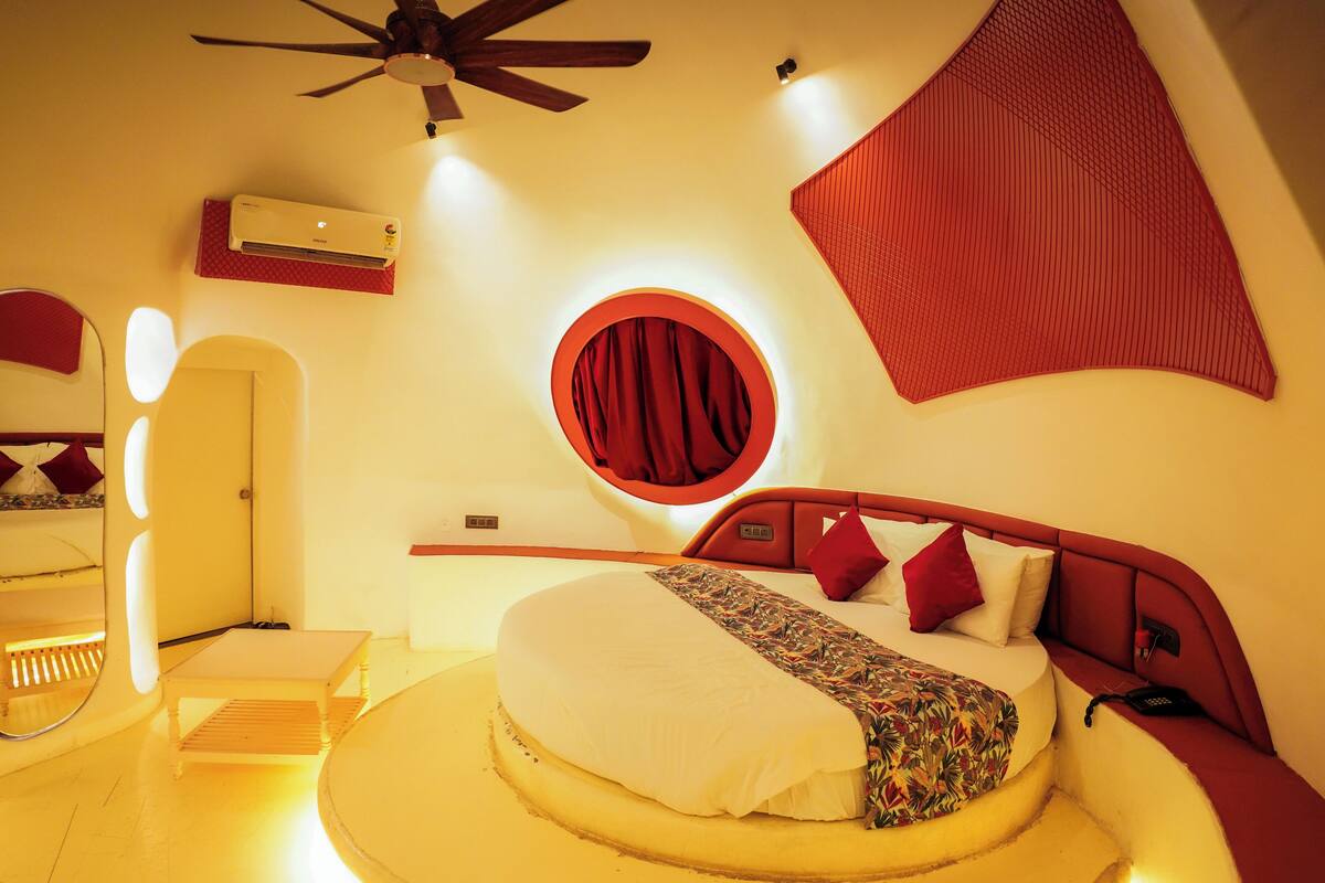 A circular bed with a red curtain, a ceiling fan, and a wall-mounted air conditioner.