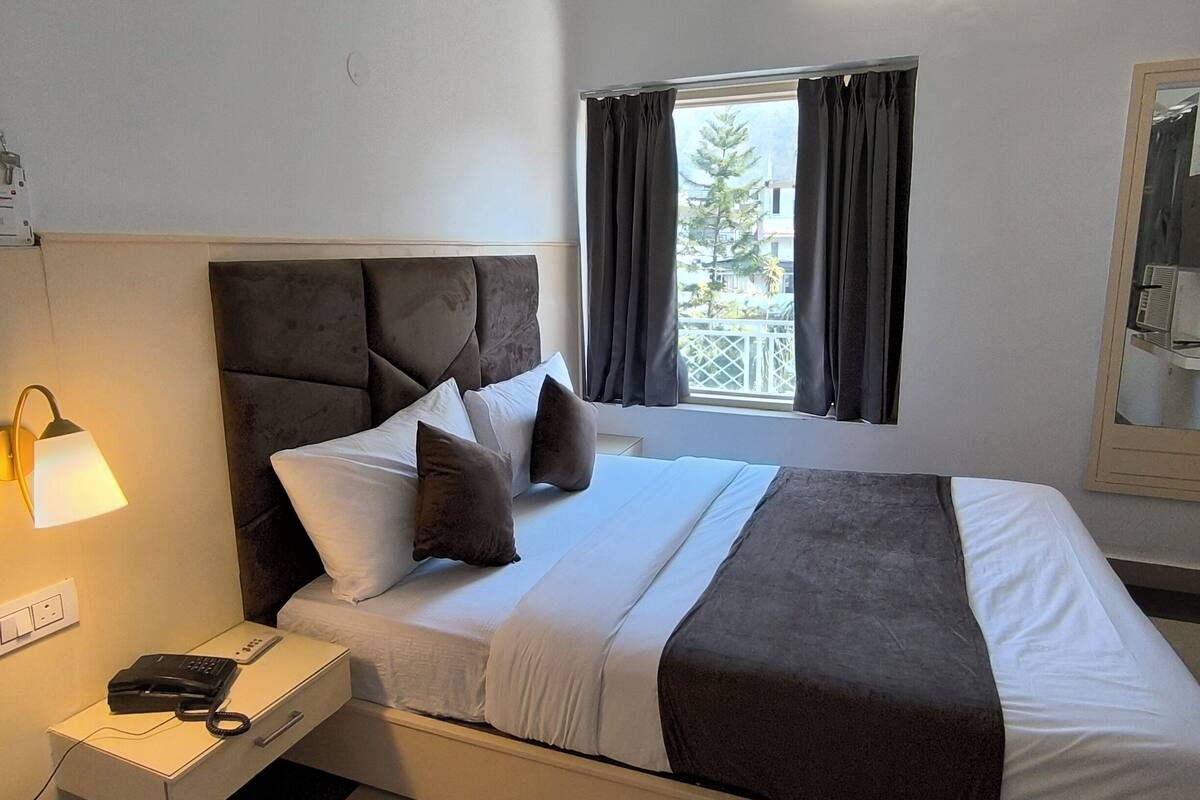 A modern hotel room with a large bed, a bedside lamp, a phone, and a window with curtains.