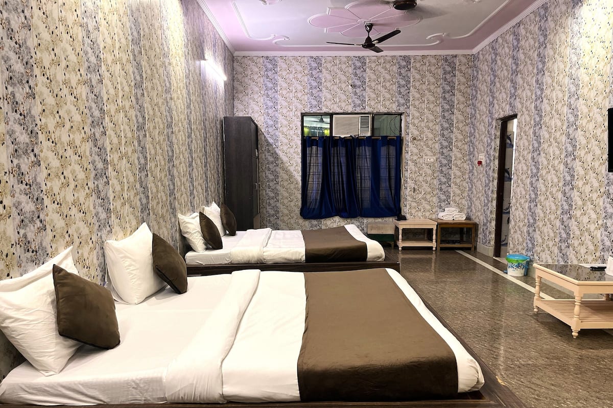 A hotel room with four beds, a ceiling fan, a window with curtains, and a small table with a towel.
