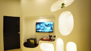 A modern bathroom with a curved sink, a black door, a flat-screen TV mounted on the wall, and a small plant on the wall. - Shridhar Reesort (Rishikesh)