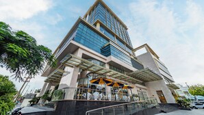 A modern hotel with a prominent glass facade, a central entrance with steps, and outdoor umbrellas. - Cosmo Stars Hotel Bac Lieu (Bac Lieu)