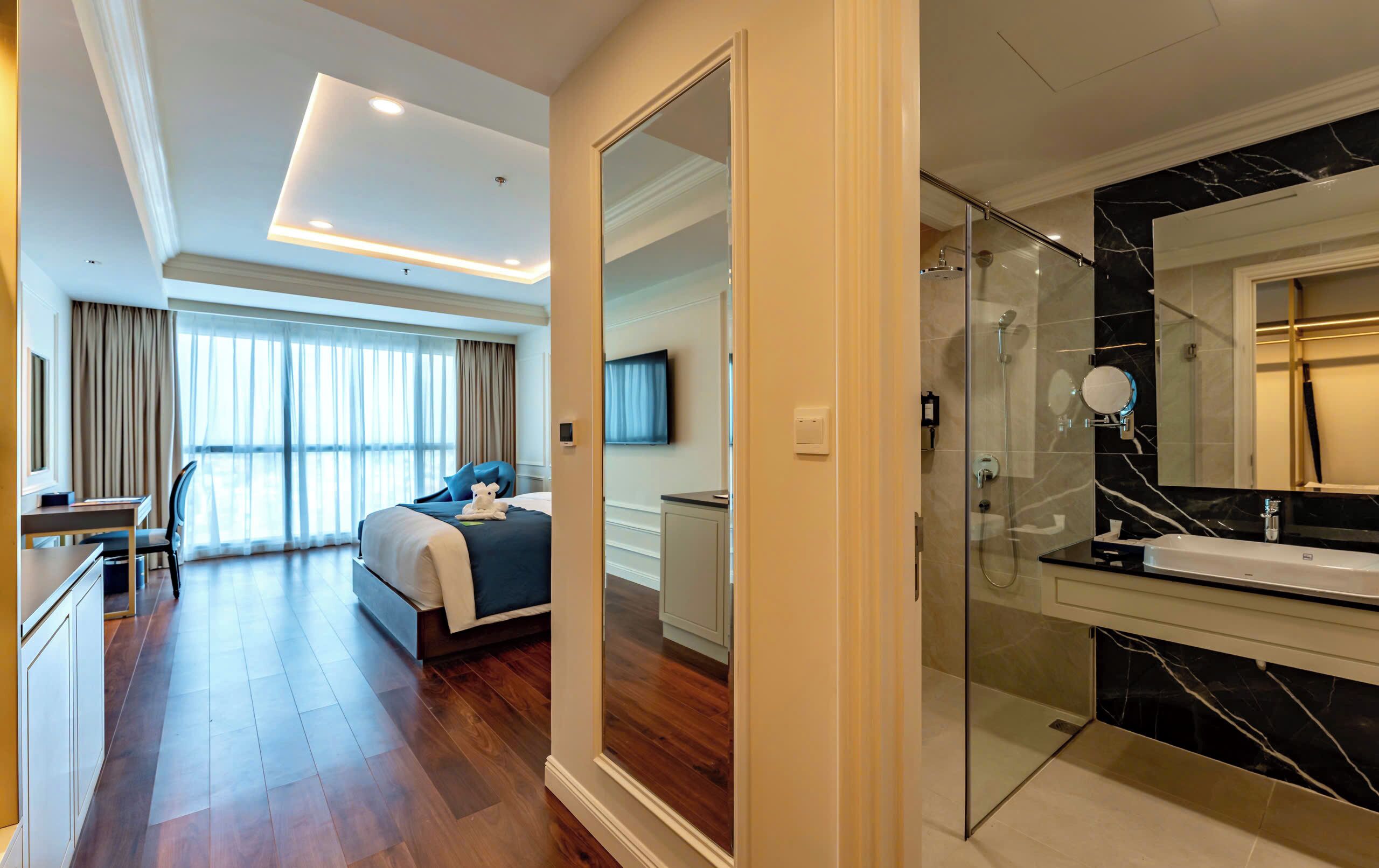 A modern hotel room with a large bed, a desk, and a bathroom with a glass shower.