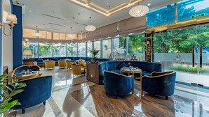 A modern lobby with blue and yellow seating, large windows, and a glass wall offering a view of greenery. - Cosmo Stars Hotel Bac Lieu (Bac Lieu)