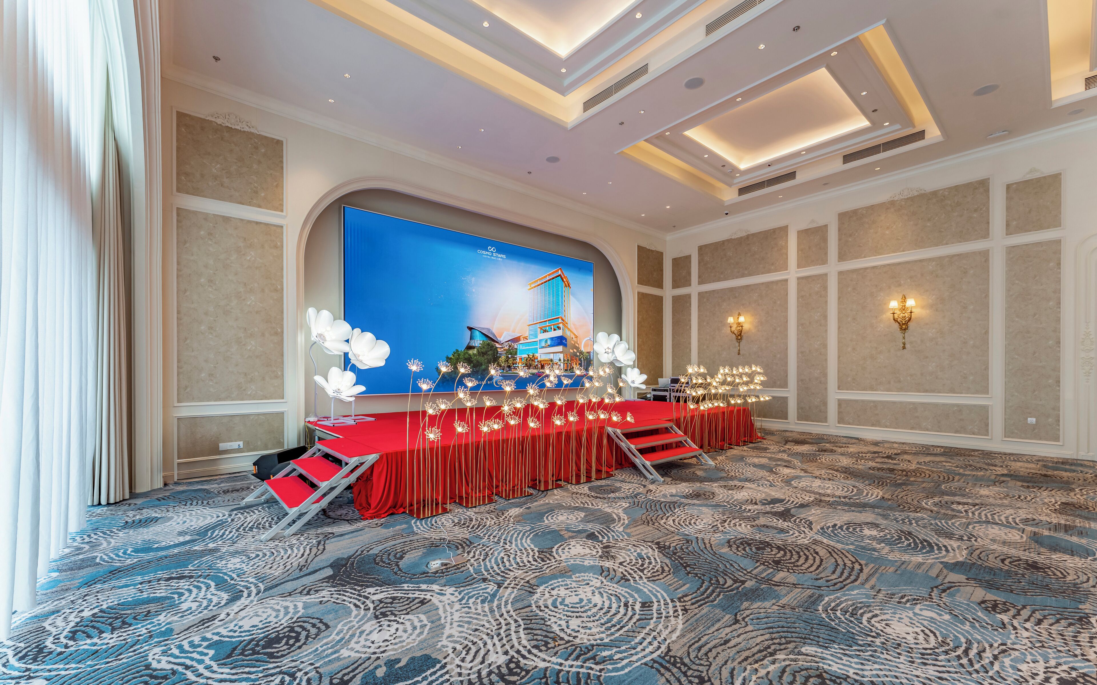 Un salón de conferencias con un escenario, alfombra roja y un suelo estampado.