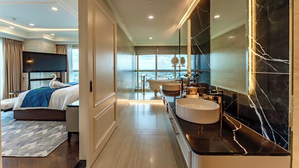 A modern hotel room with a large bed, a separate bathroom with a bathtub, a large mirror, and a view of the city. - Cosmo Stars Hotel Bac Lieu (Bac Lieu)
