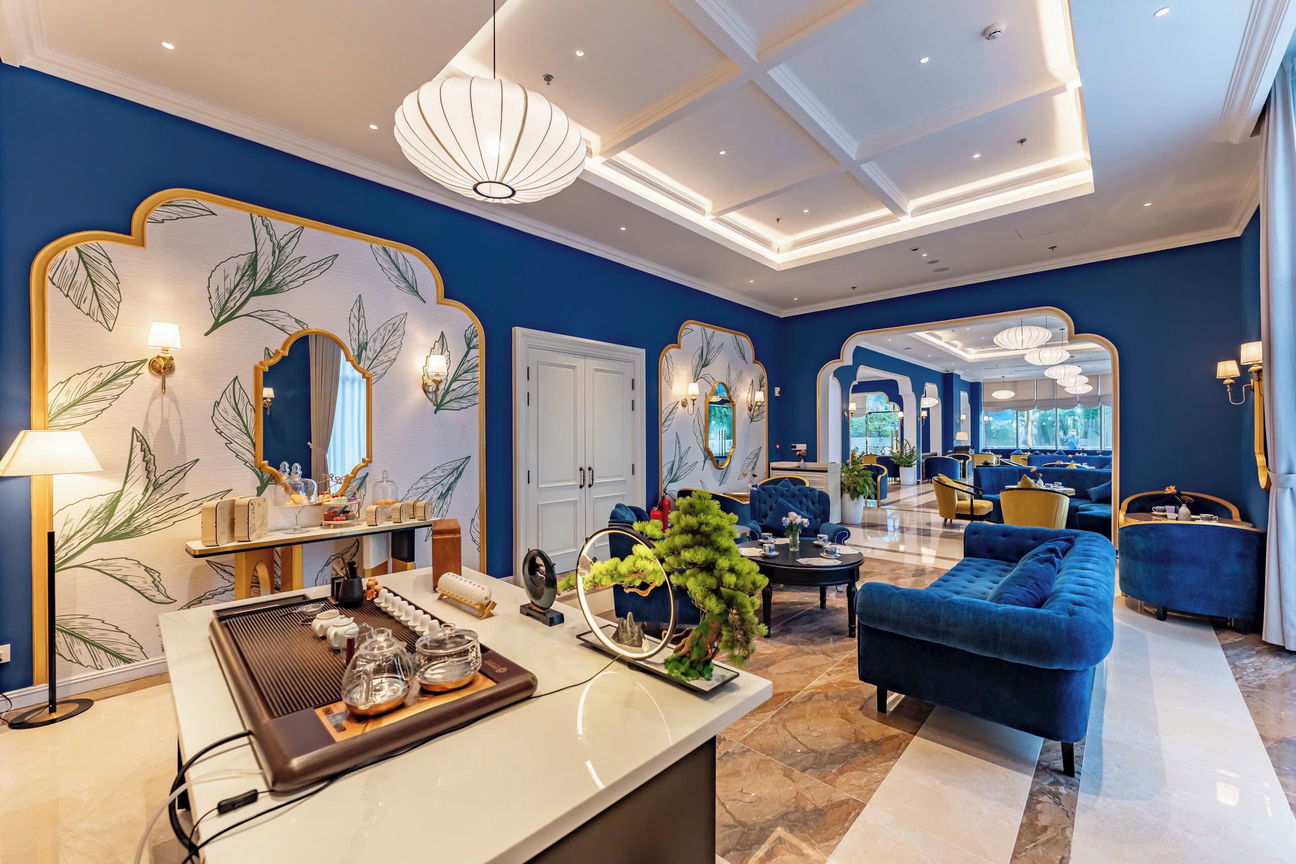 A modern hotel lobby with a blue wall, large mirrors, and a seating area with blue sofas.