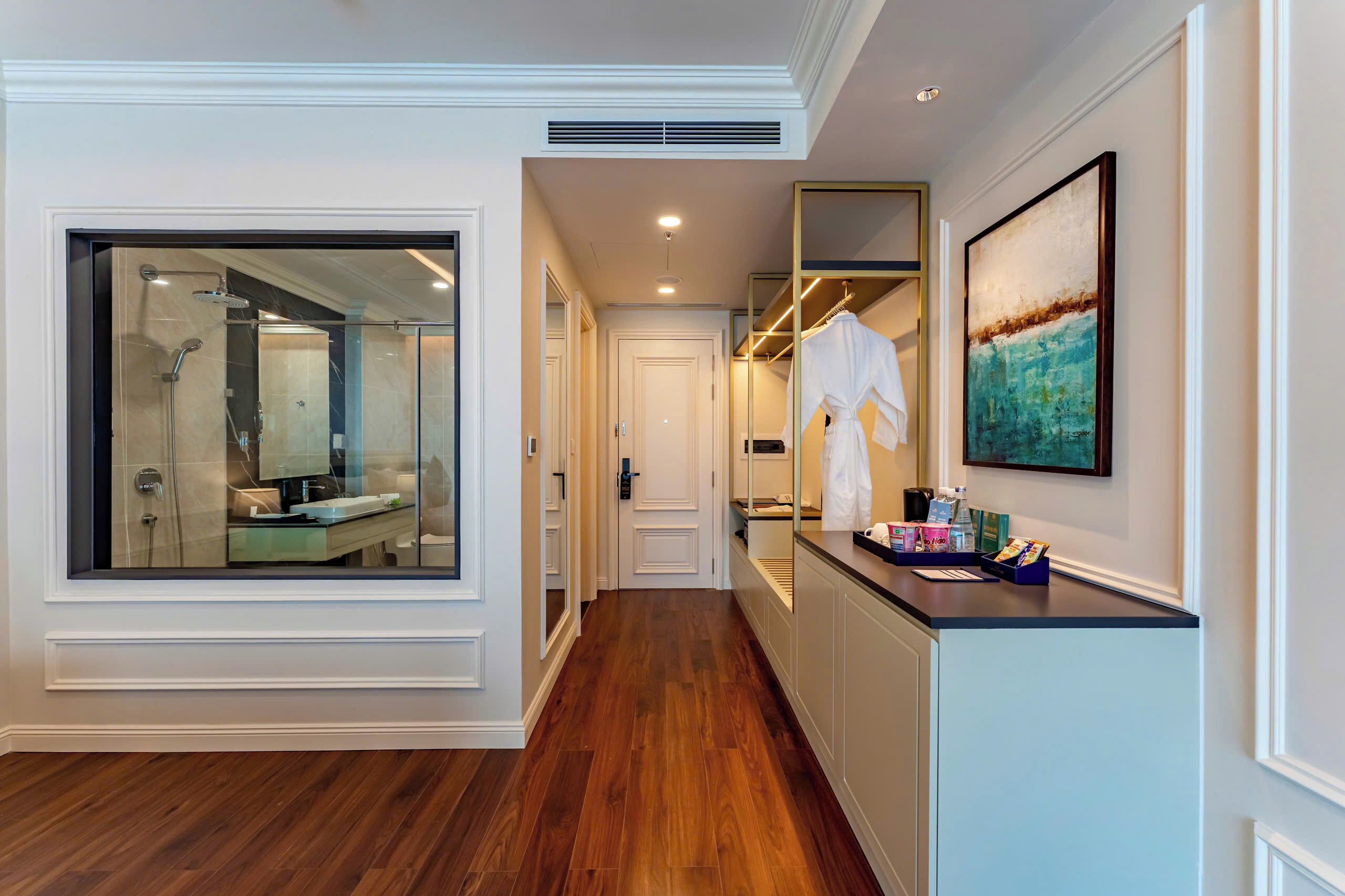 A hallway with a glass-enclosed shower, a mirror, a robe hanging on a rack, and a painting on the wall.