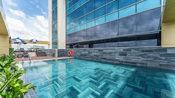 Et moderne poolområde med en klar, blå pool, liggestole og parasoller.
