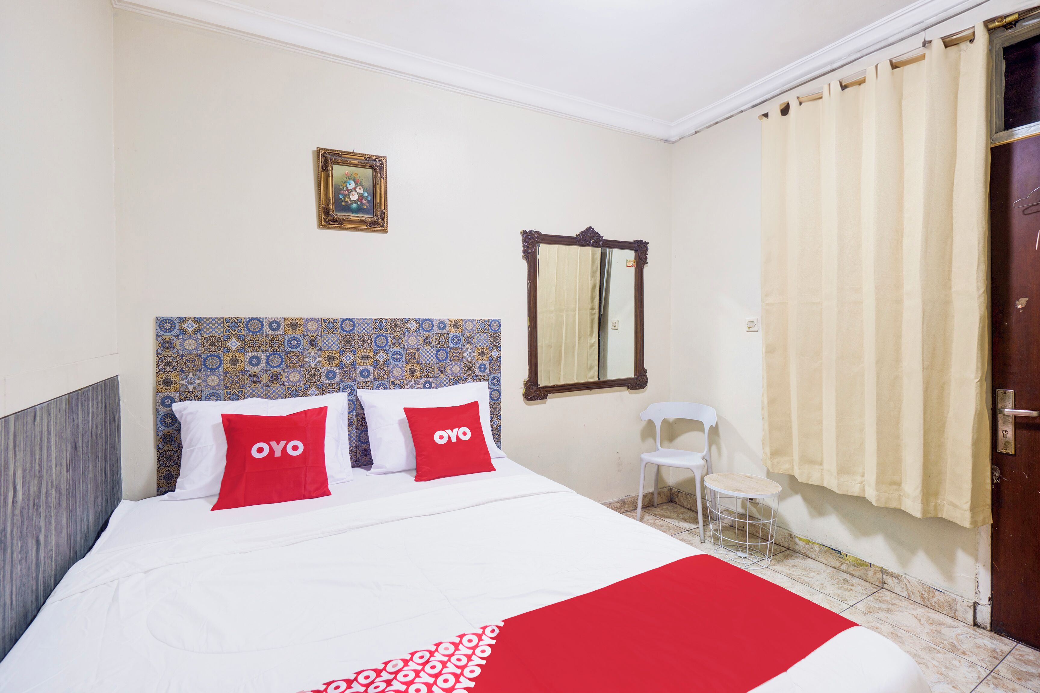 Une chambre d’hôtel avec un lit, une chaise, une petite table, un miroir et une porte.