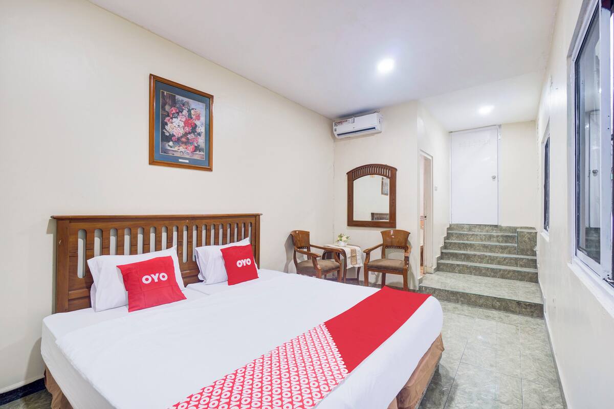 Une chambre d’hôtel avec un lit, un bureau, une chaise, un miroir et un escalier.