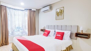 Hotelkamer met een bed, gordijnen, een airconditioner, een wandlamp en een raam met uitzicht.