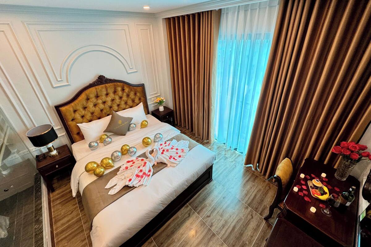 A hotel room with a large bed, a nightstand, a desk with a chair, and a window with curtains.