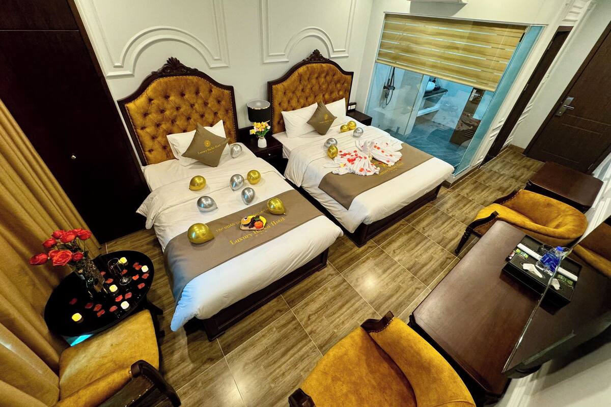 A hotel room with two beds, a sitting area, a small table, and a view of a pool.