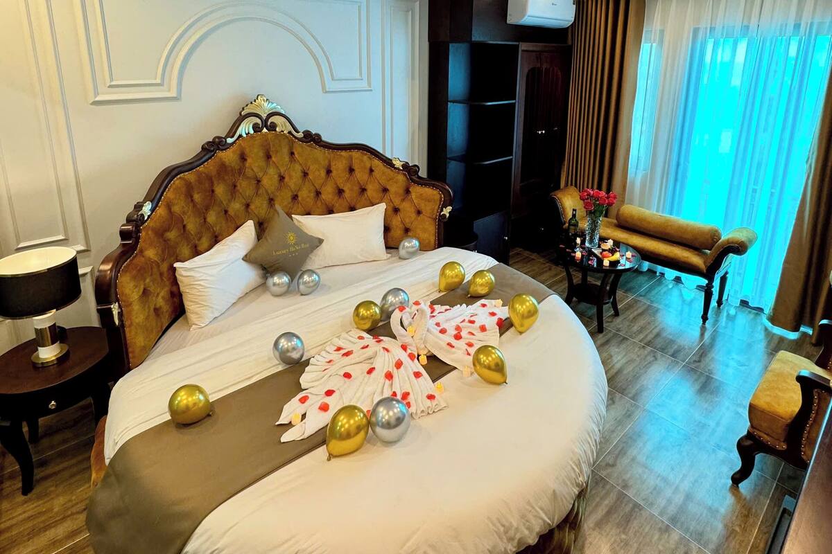 A luxurious bedroom with a large bed, a nightstand, a dresser, and a seating area with a table and chairs.