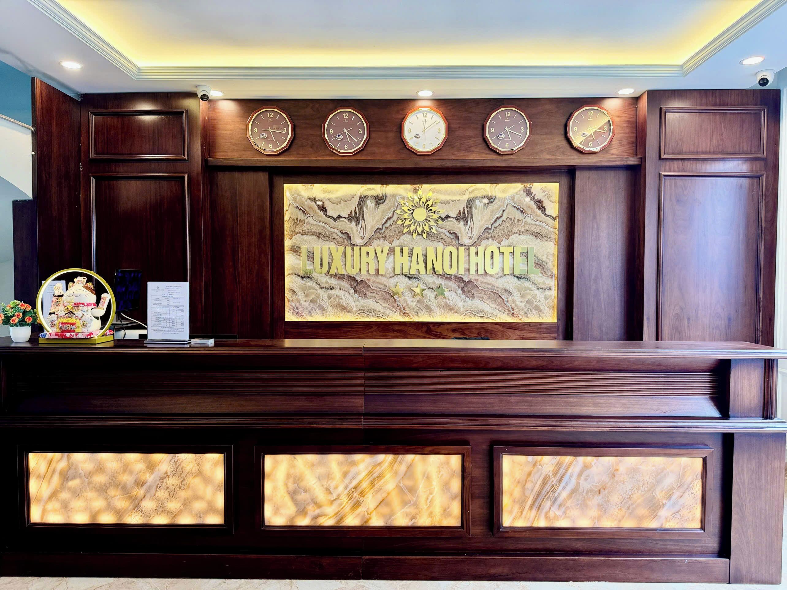 A reception desk with a large sign reading "LUXURY HANOI HOTEL" and multiple clocks above it.