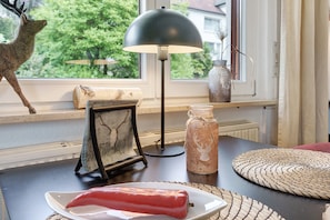 Een tafel met een lamp, een hertenbeeldje, een lijst met foto, een pot en een geweven placemat.