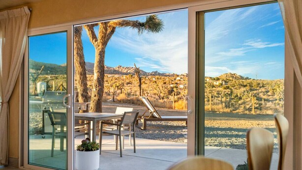 A room with a sliding glass door leading to an outdoor patio with a table, chairs, and a grill. - Wind View Pioneertown (Pioneertown)