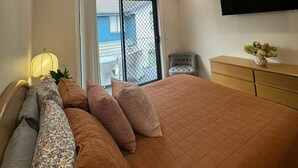 A bedroom with a large bed, a ceiling fan, a flat-screen TV, and a sliding glass door to the outside.