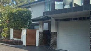 A modern two-story house with a white garage door, a balcony with wicker furniture, and a gated entrance.