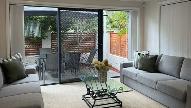 A modern living room with a grey sofa, a glass coffee table, and a sliding glass door leading to a patio.