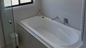 A modern bathroom with a large bathtub, a window, and a glass shower enclosure.