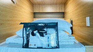 A compact hotel room with wooden walls and a single bed. A plastic bag containing toiletries is placed on the bed. - Amango Hostel (Ho Chi Minh City)