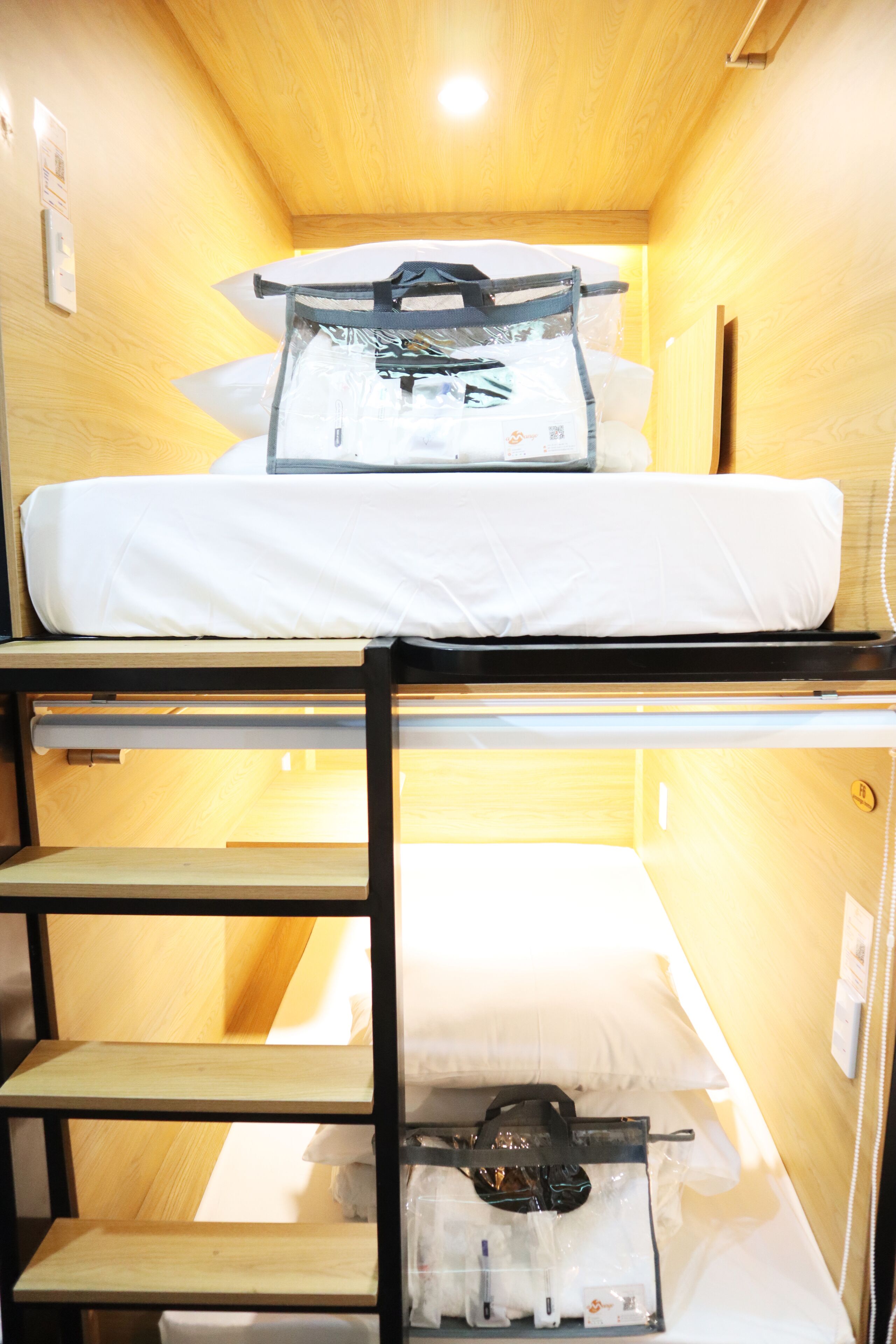 Un lit superposé avec un matelas et des oreillers, une étagère avec un sac, et un téléphone fixé au mur.