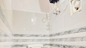 Une salle de bain équipée de toilettes, de carreaux de marbre, d’une douche et d’un sèche-mains fixé au mur.