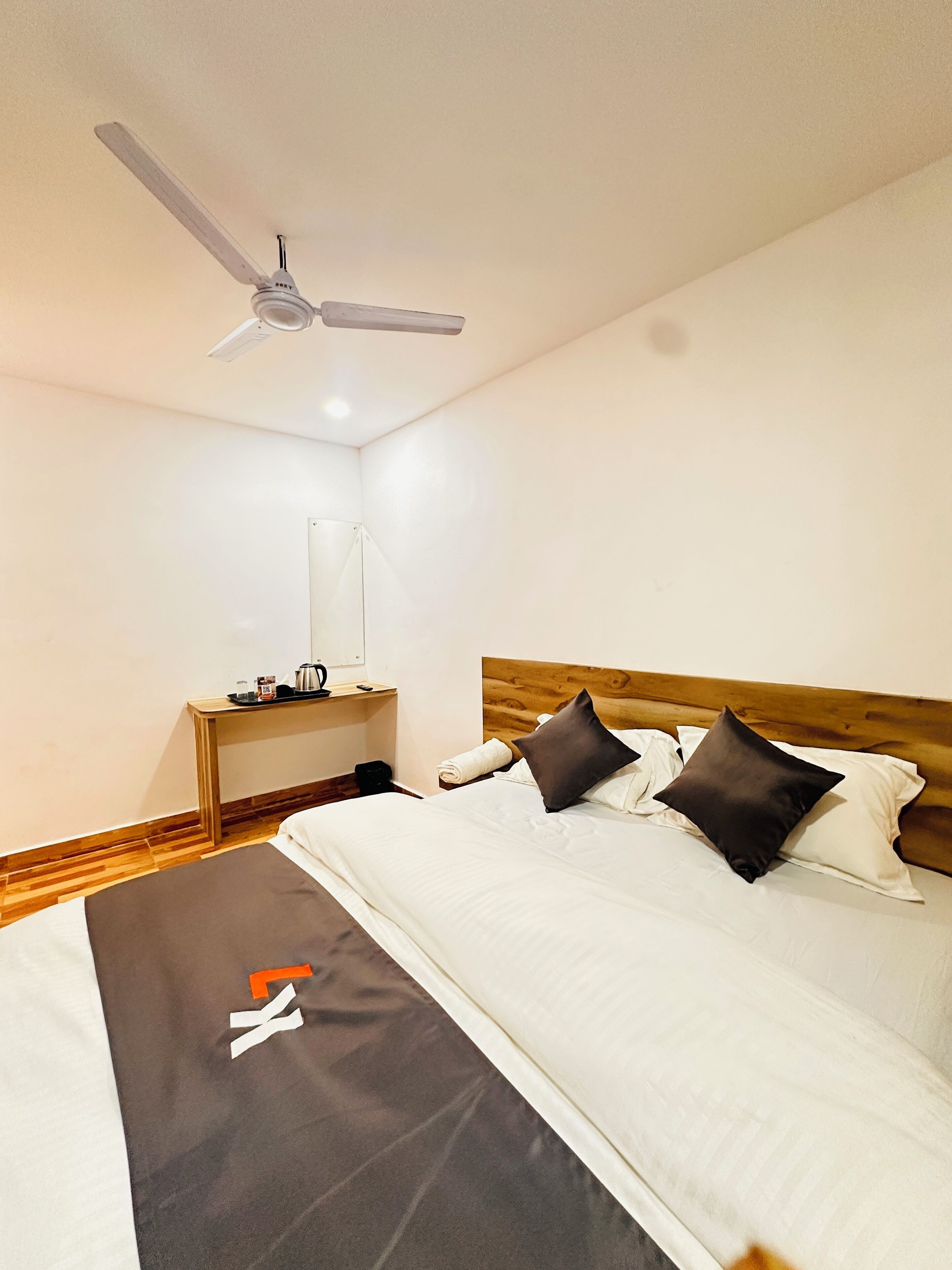 Una habitación de hotel con una cama, una mesita de noche, un ventilador de techo y un espejo.