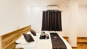 Un lit bien fait, avec une tête de lit en bois, une table de chevet sur laquelle est posée une serviette, un ventilateur de plafond et une fenêtre avec des rideaux.