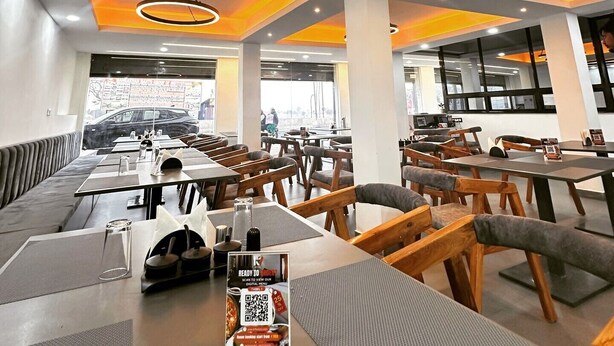 Un restaurant moderne avec de hauts plafonds, des luminaires suspendus de forme circulaire et un mélange de sièges en bois et de sièges rembourrés. Les tables sont dressées avec des verres et des menus.