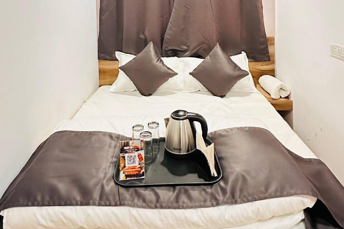 A neatly made bed with a tray of breakfast items, a kettle, and glasses on a bedside table.