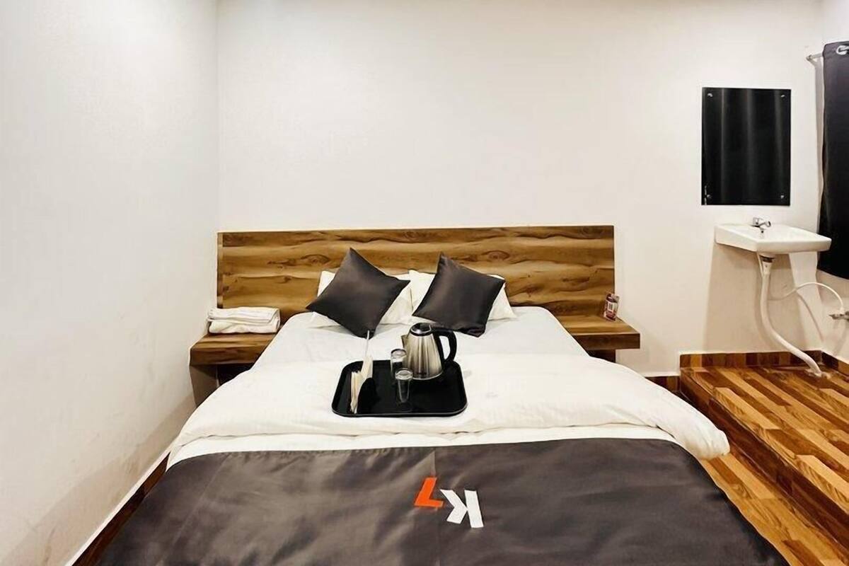 A hotel room with a bed, a bedside table, a nightstand, a ceiling fan, a window, and a sink.