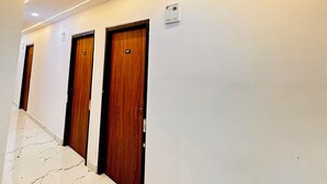 Un couloir avec trois portes en bois, une caméra de surveillance et un plafond doté d’un éclairage encastré.