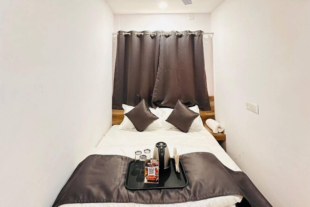 A narrow hotel room with a bed, a ceiling fan, and a nightstand with a phone and a tray of breakfast items.