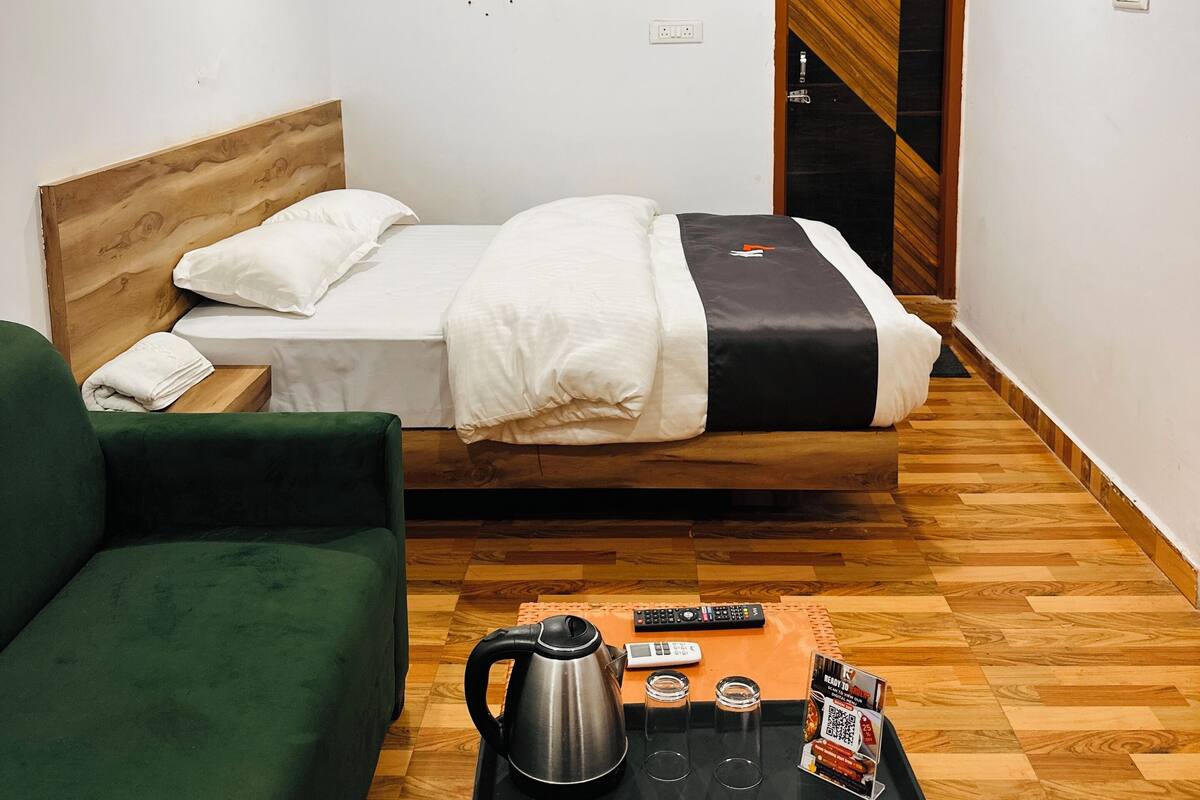A hotel room with a bed, a green sofa, a coffee table with a kettle, glasses, and a remote control.