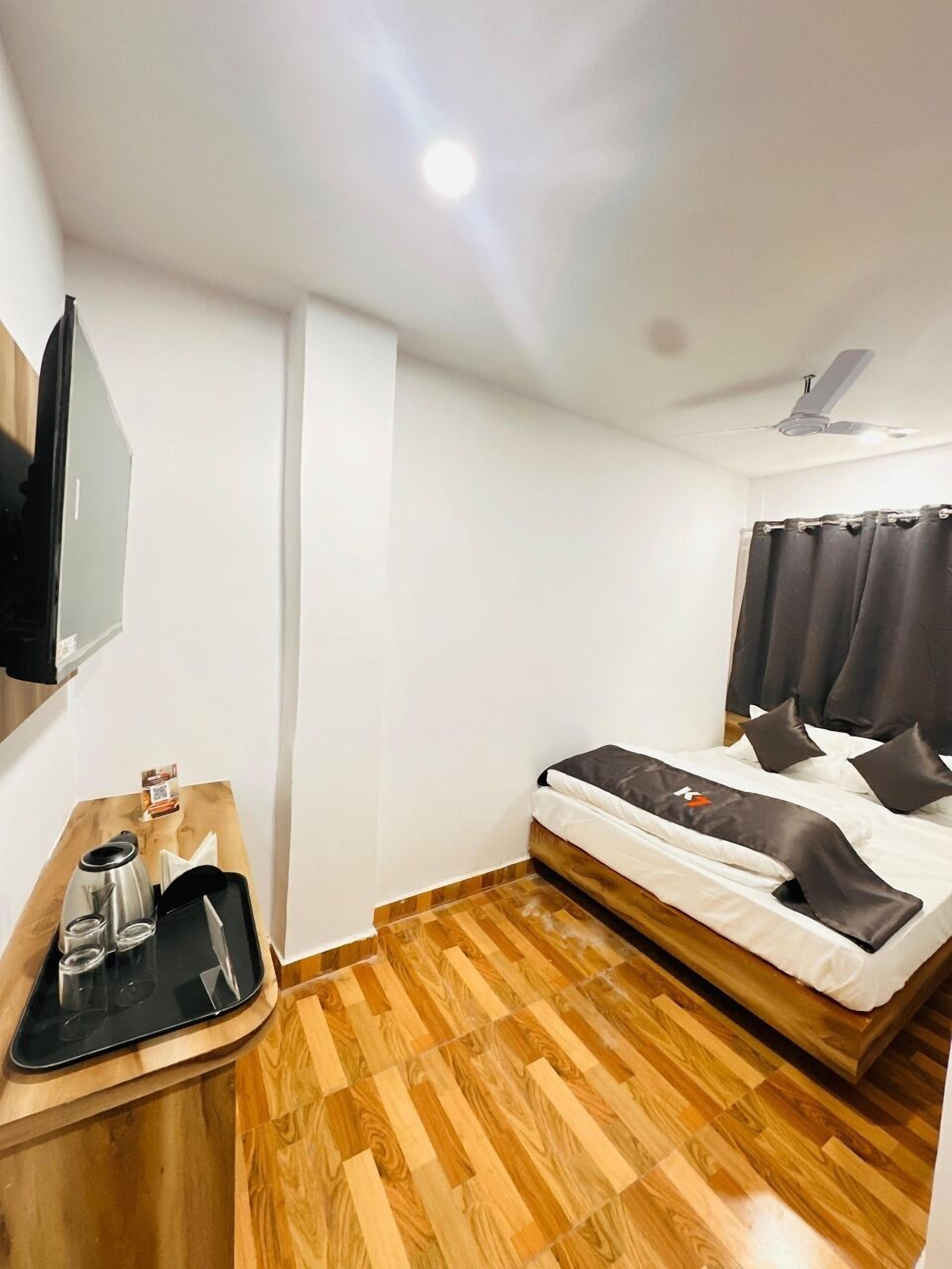 A hotel room with a bed, a flat-screen TV mounted on the wall, a wooden side table with a tray, and a ceiling fan.