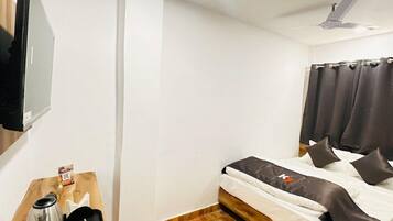A hotel room with a bed, a flat-screen TV mounted on the wall, a wooden side table with a tray, and a ceiling fan.