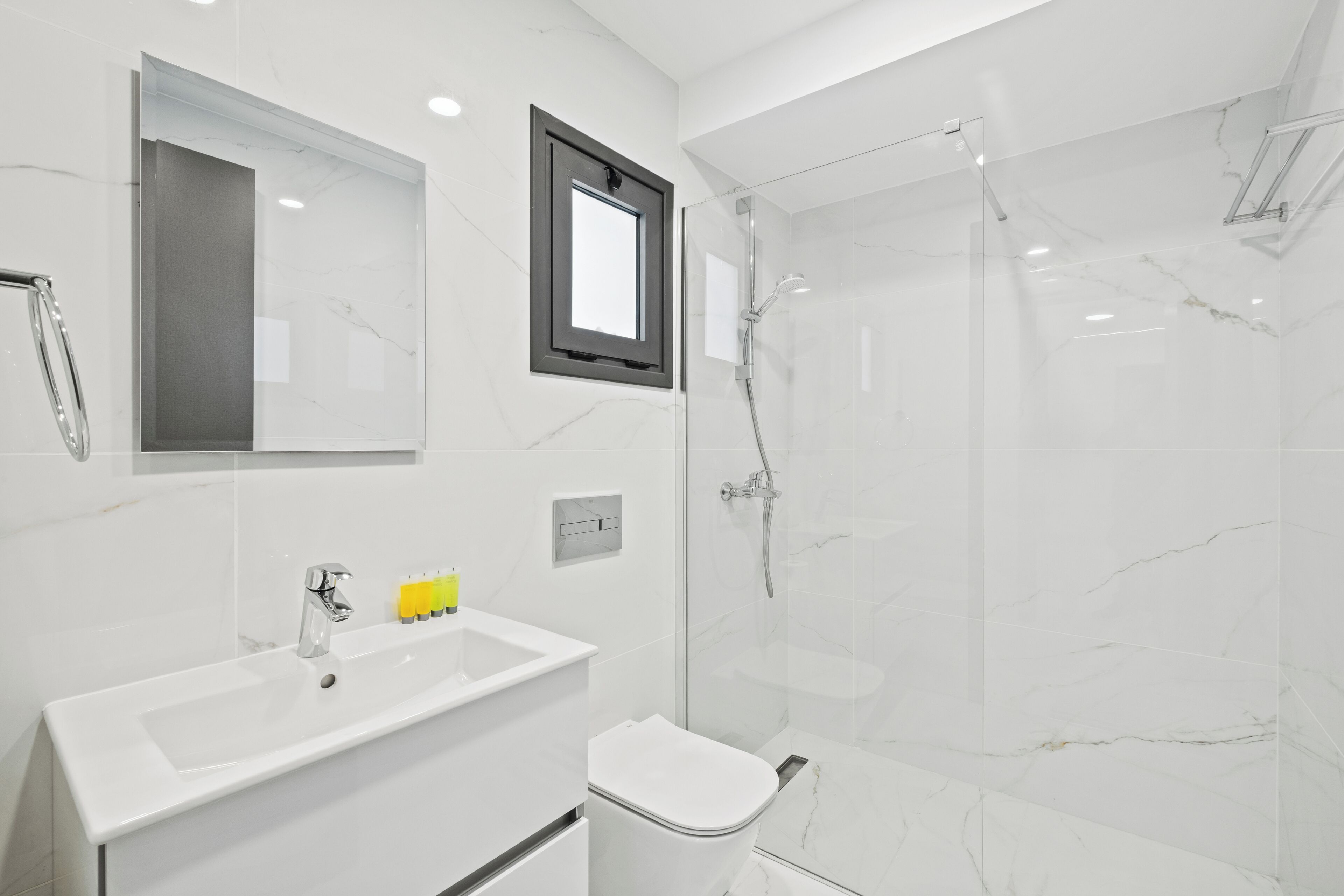 Un baño moderno con lavamanos blanco, espejo y cabina de ducha con mampara de vidrio.