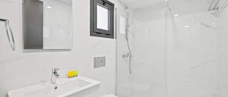 Un baño moderno con lavamanos blanco, espejo y cabina de ducha con mampara de vidrio.