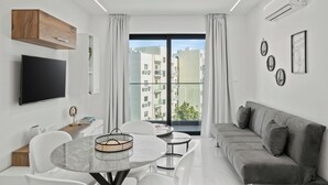 Una sala de estar moderna con un televisor de pantalla plana, un sofá gris, una mesa de comedor con sillas y un ventanal con vistas a la ciudad.