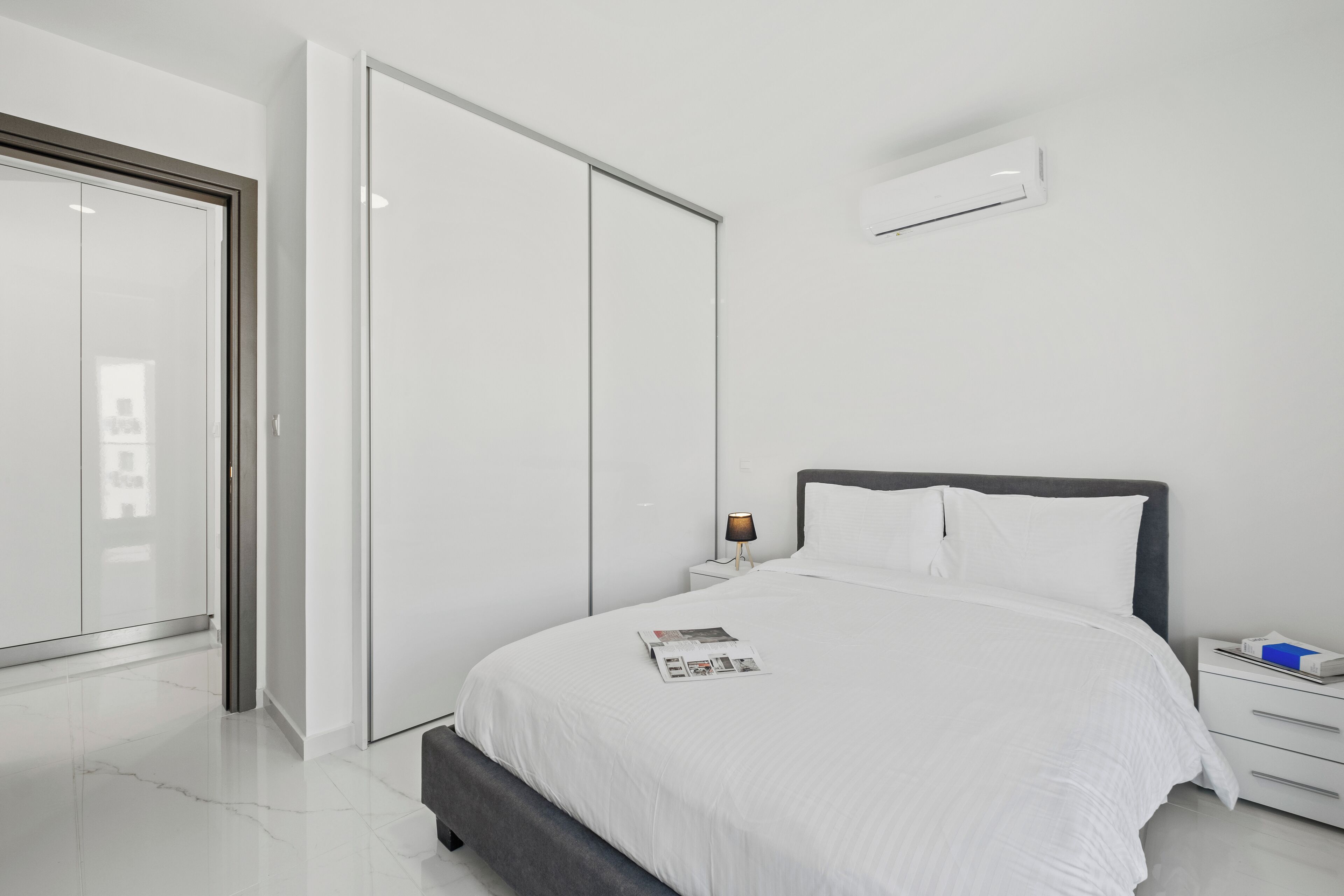 Une chambre moderne avec un grand lit, une table de chevet, une lampe et une armoire.