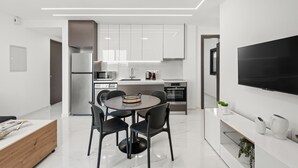 Una cocina moderna con armarios blancos, un comedor con una mesa redonda y sillas, y un televisor de pantalla plana montado en la pared.