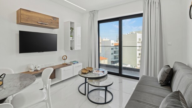 Un salón moderno con televisor de pantalla plana, una mesa de comedor, un sofá y un ventanal con vistas a la ciudad.