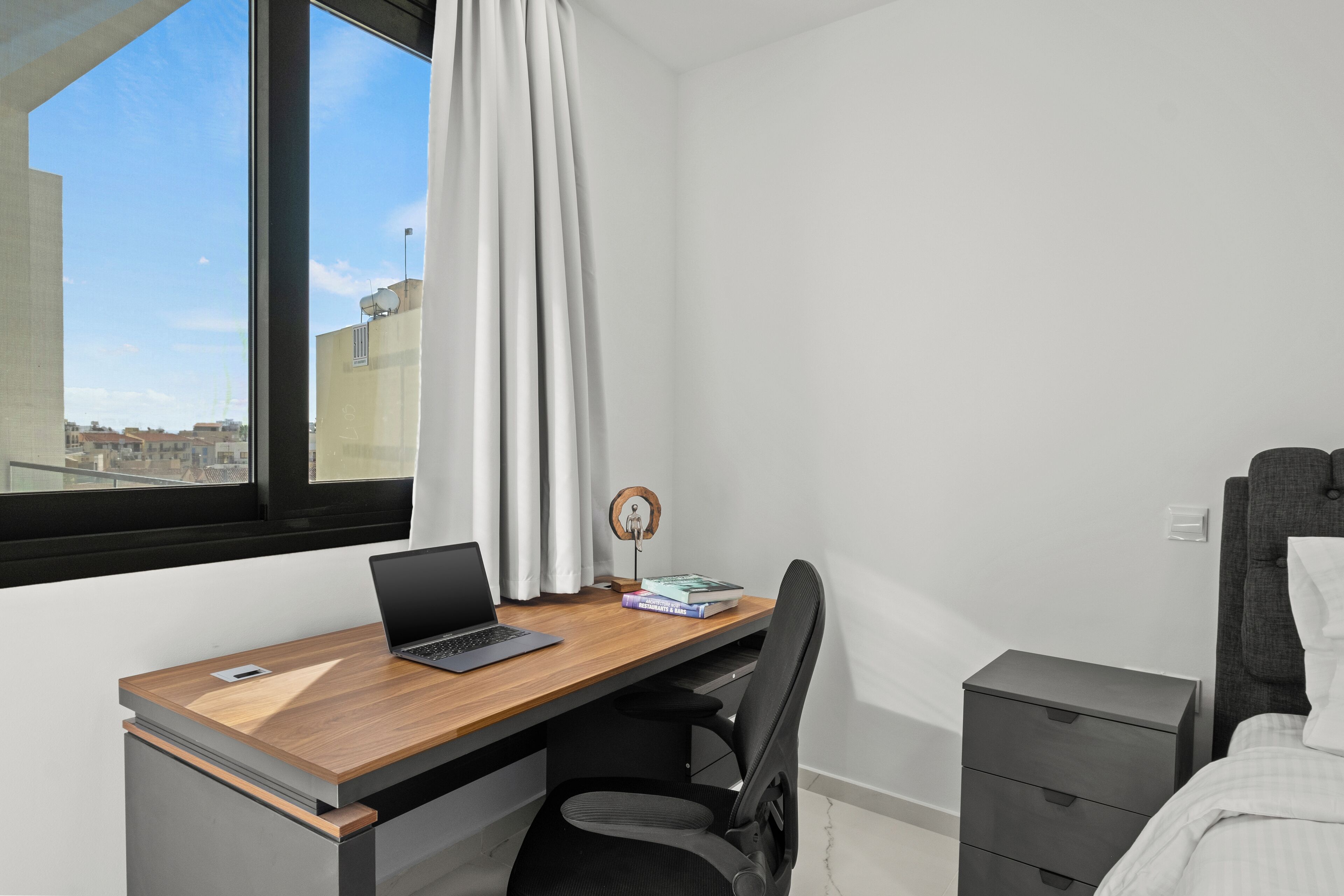 Une chambre à coucher moderne avec un bureau en bois, un ordinateur portable, une chaise, une table de chevet et un lit.