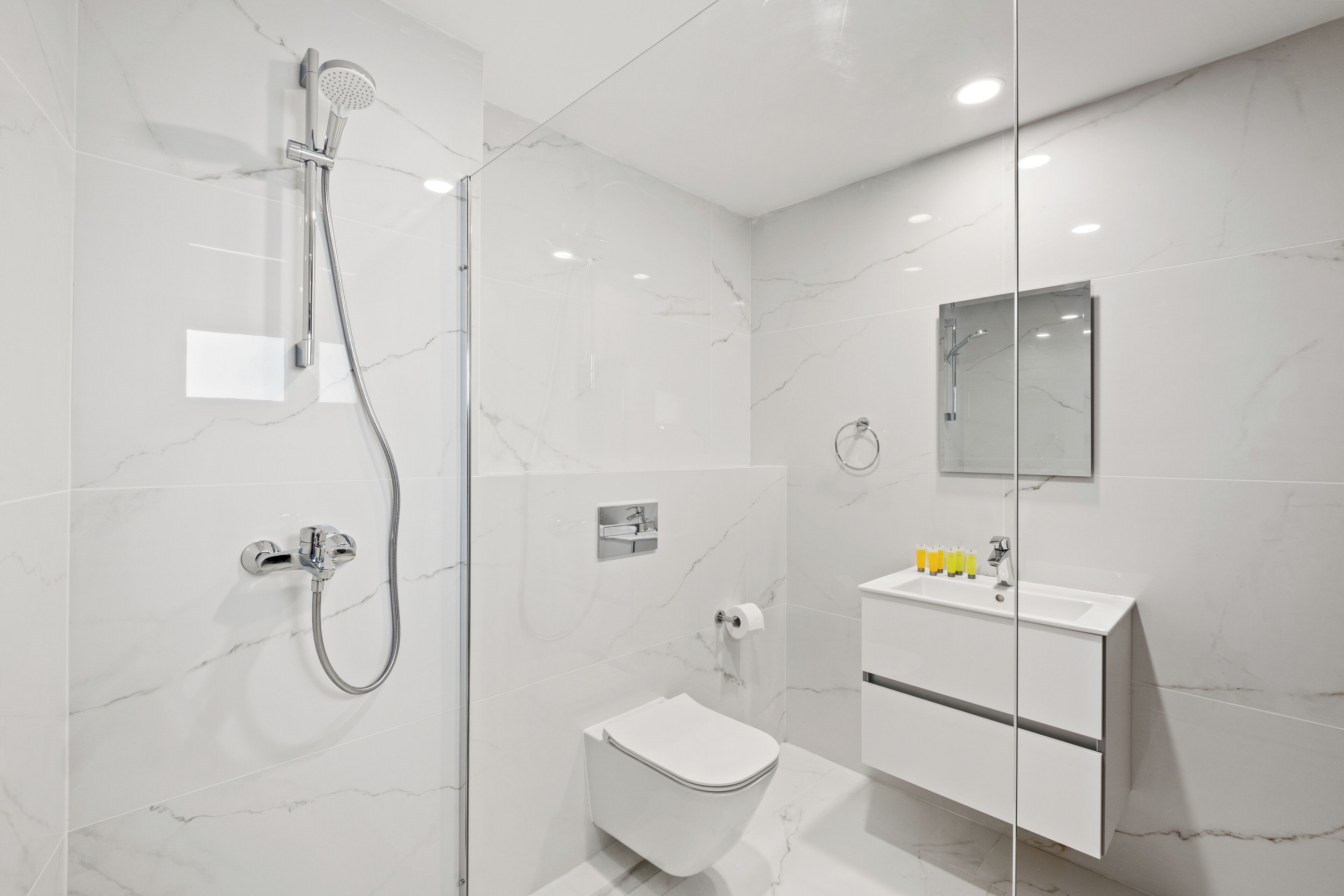 A modern bathroom with a glass shower enclosure, a white toilet, and a white sink with a mirror above it.